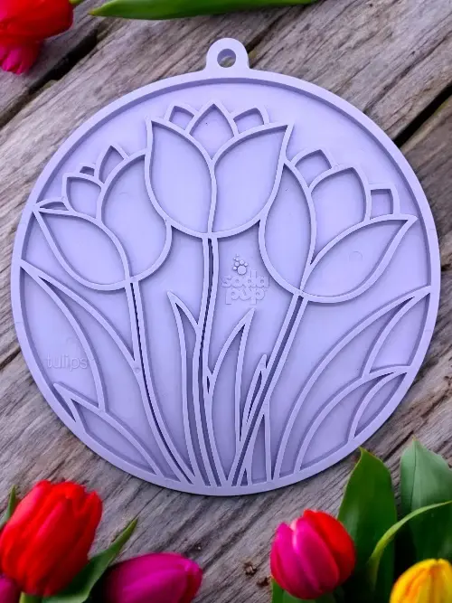 Lilla SodaPup slikkemåtte med tulipan-design ligger på et rustikt træbord omgivet af friske tulipaner i forskellige farver.