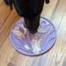 En sort hund slikker intenst på en lilla SodaPup Tulipan slikkemåtte placeret på et trægulv
